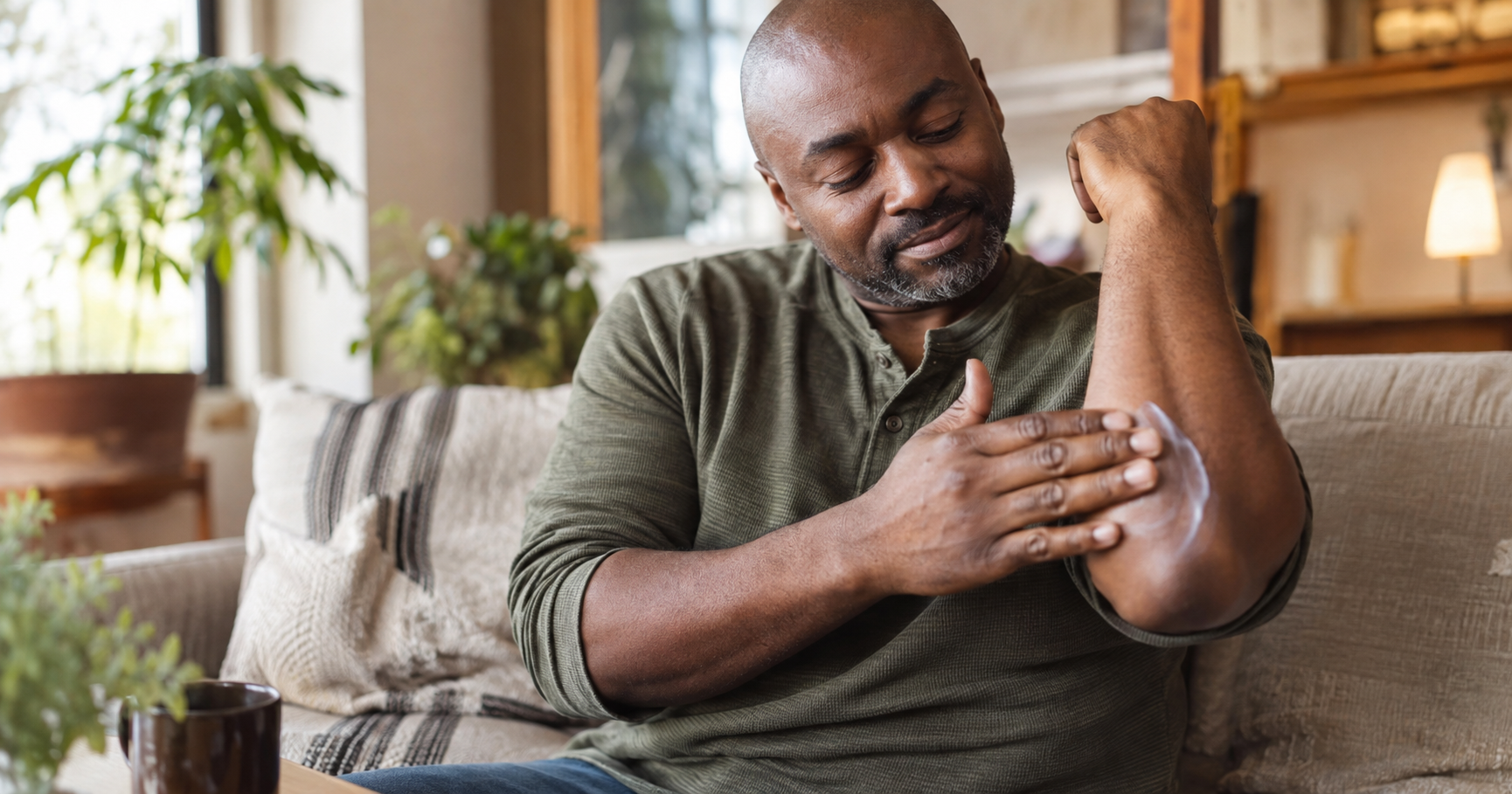 Man with dark brown skin applying cream to his arm as part of his psoriasis care routine
